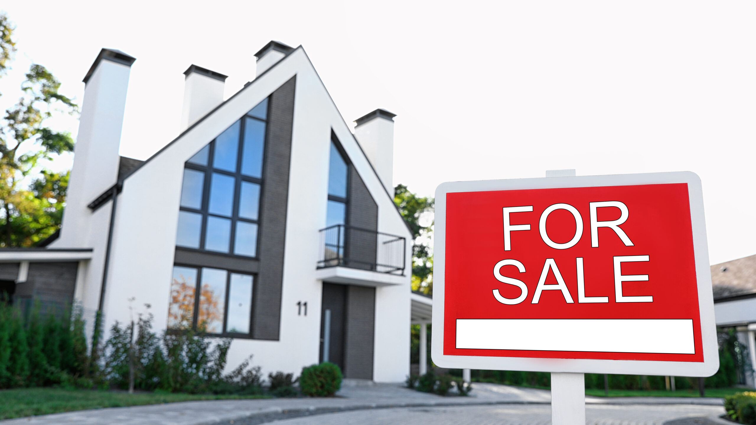 Red real estate sign near house outdoors on sunny day